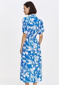 Niebieska i biała sukienka w kwiaty z krótkimi bufkami, zapięciem na guziki przy kołnierzyku, talią ściągniętą w pasie oraz długością do połowy łydki, wykonana z lekkiego materiału.