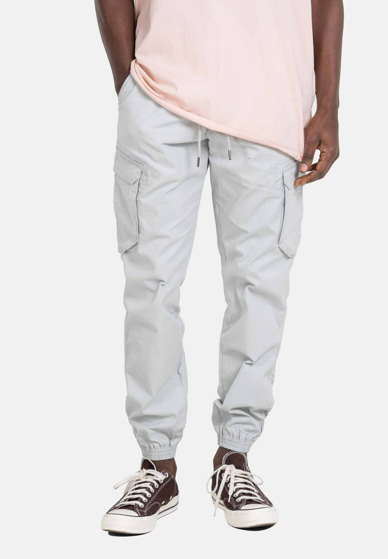 Pantalones cargo de color gris claro con puños elásticos y cintura con cordón, que cuentan con bolsillos laterales y una tela suave y ligera. Combinados con zapatillas oscuras.