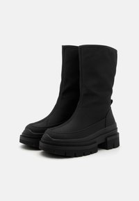 Black ankle boots made of fabric with a chunky rubber sole, featuring a tall shaft, rounded toe, and minimal seam detailing.
