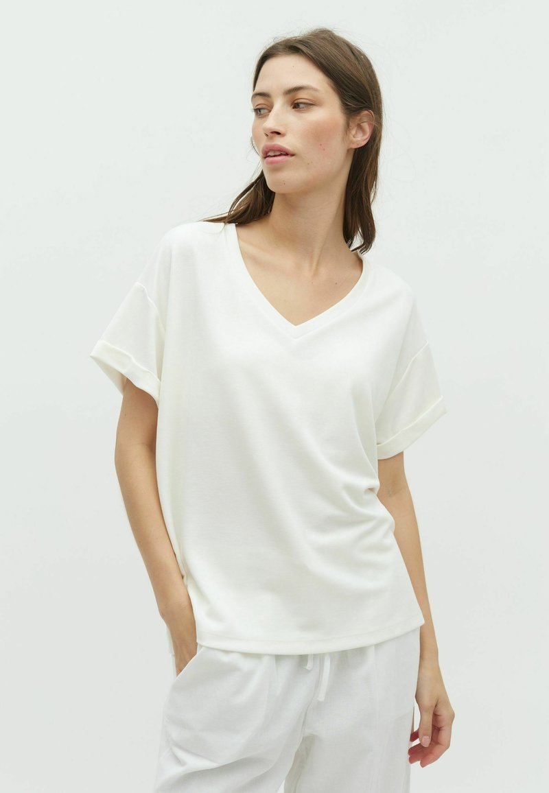 Camiseta blanca de cuello en V con mangas cortas enrolladas, hecha de tejido suave, con un corte relajado y una textura suave.