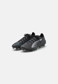 Botas de fútbol negras con una parte superior sintética texturizada, que presentan detalles en turquesa, cordones tradicionales y tacos moldeados para mayor tracción.