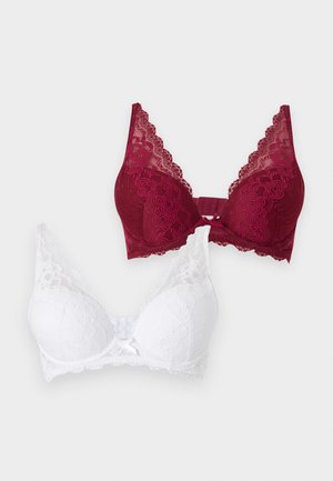 Δύο δαντελωτά σουτιέν, ένα βαθύ κόκκινο και ένα λευκό, και τα δύο με floral σχέδια και λεπτομέρειες με φιογκάκια μπροστά, τοποθετημένα σε απλό φόντο.