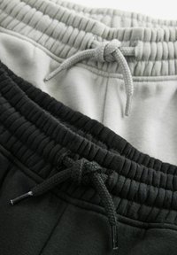 Twee paar sweatpants: één grijs en één zwart. Beide hebben een elastische tailleband met bijpassende trekkoord en een gestructureerde stof.