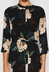 Czarna sukienka w kwiaty z rękawami o długości trzech ćwiartek, z dużymi kremowymi i brązowymi kwiatami, zielonymi liśćmi, button-up z przodu oraz wiązanym w pasie.