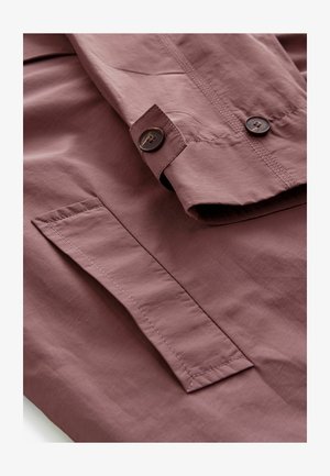 Šviesiai purpurinė striukė, pasižyminti lygiu, tekstūruotu audiniu. Su sagų užsegimu ir kišene priekyje su kontrastinga siūle.