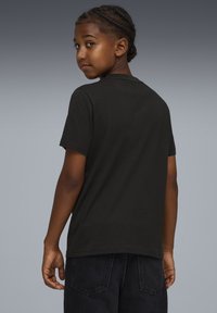 Musta lyhythihainen T-paita, pyöreä kaulus, puuvillakangasta, rento malli, yksinkertainen muotoilu, tumma farkkuhousut, näkymä takaa.