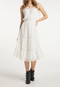 Weißes, gestuftes Midikleid mit Spitzenakzenten am Saum und am Ausschnitt, ausgestattet mit verstellbaren Spaghettiträgern, kombiniert mit schwarzen Knöchelstiefeln.