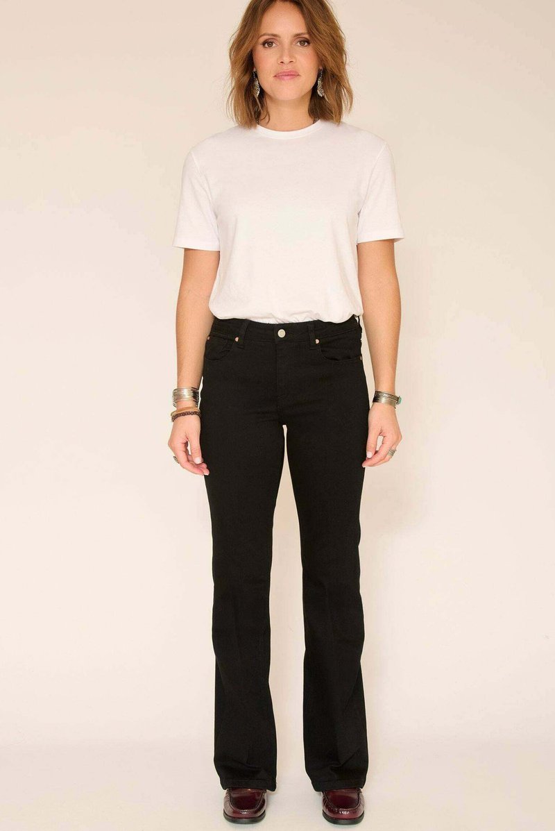 Jean évasé taille haute noir en denim, avec des poches avant, une silhouette ajustée et des détails de couture subtils. Associé à un t-shirt blanc.