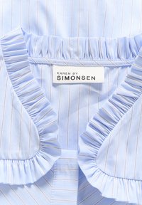 Vaaleansininen paita, jossa on valkoisia ja ruskeita pystysuoria raitoja. Rypytetty kaulus. Labelin teksti: "KAREN BY SIMONSEN". Silkkinen kankaan pinta.