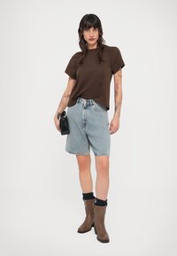 Καφέ κοντομάνικη μπλούζα, ανοιχτό μπλε τζιν σορτς, καφέ μποτάκια μέχρι τον αστράγαλο με μαύρες κάλτσες και μια μικρή μαύρη τσάντα. Απλή καθημερινή εμφάνιση.