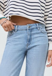 Svetlo modri jeans iz denima s ravnim krojem, subtilnimi okrasnimi elementi in zapiranjem na gumb. V kombinaciji s skrajšano puloverjem s črtami.