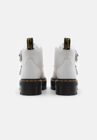 Botas de tobillo de cuero blanco con un acabado texturizado, suela gruesa negra y costuras amarillas. Presenta dos correas ajustables y una lengüeta de tirón.