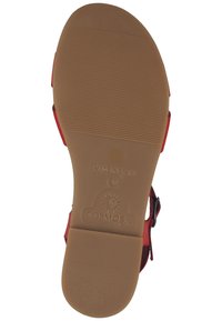 Brun gummisål med vandrette riller, røde stropper til sikring af foden og branding præget med et sol-logo, markeret "Made in Spain."