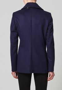 Sako ze směsi vlny v námořnické modři s přiléhavým střihem, ostrými klopami a jedním knoflíkem u krku. Hladká textura a čisté linie.