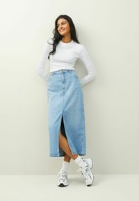 Ljust blå denimmaxikjol med en framfåra, bärs med en vit långärmad skjorta och vita sneakers, med en avslappnad passform och hög midja.