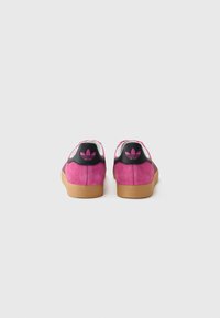 Pink suede sneakers with a black heel cap featuring a pink logo, white accents, and a textured gum rubber sole.