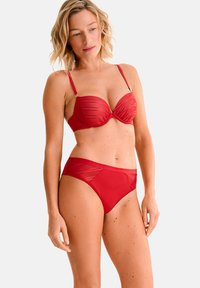 Ensemble de bikini rouge comprenant un soutien-gorge structuré et rembourré avec des coutures verticales et des bretelles réglables ; bas taille haute assortis avec des accents transparents.