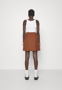 Gonna marrone, lunga fino al ginocchio, con una vita elastica, abbinata a una canotta bianca e calzini bianchi a crew. Scarpe nere con plateau completano il look.