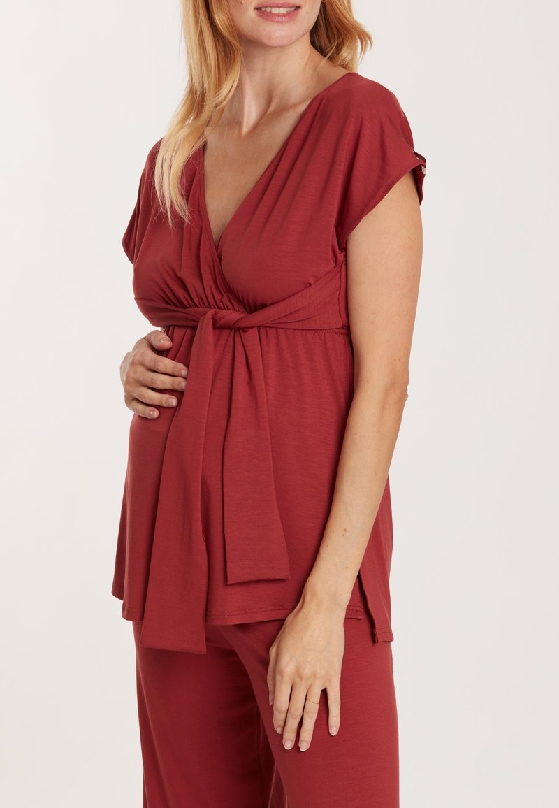 Schwangerenoberteil in tiefrot, mit V-Ausschnitt, kurzen Ärmeln und einem Bindeband in der Taille. Hergestellt aus weichem, dehnbarem Stoff für hohen Tragekomfort.