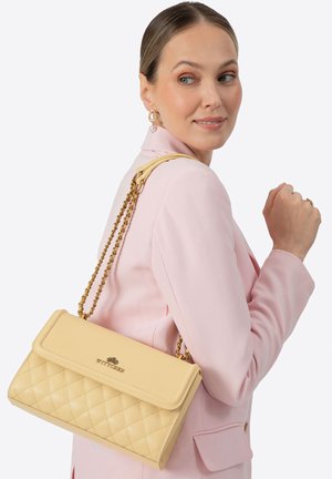 Sac à main matelassé jaune avec une bandoulière chaîne dorée et un rabat à repli. Présente un détail logo à l'avant et une texture lisse.