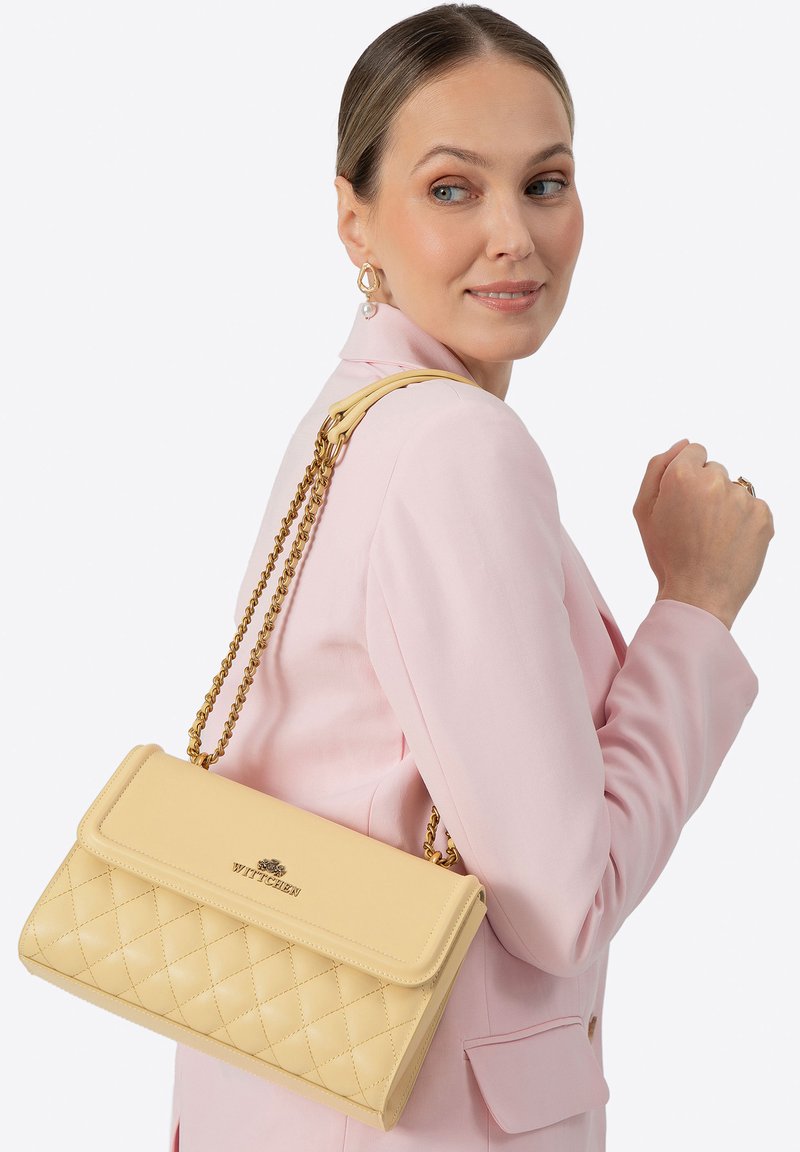 Borsa gialla trapuntata con tracolla a catena color oro e patta a risvolto. Presenta un dettaglio con logo sul davanti e una texture liscia.