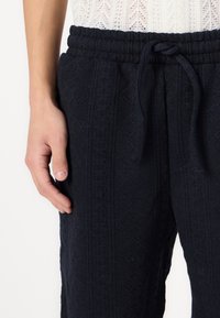 Marinblå joggers med texturerad tyg i geometriskt mönster, elastisk midja med dragsko och sidofickor.