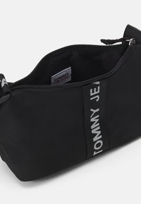 Black fabric pouch with a zip closure, featuring a white "TOMMY JEANS" logo on the front and smooth texture. Interior view visible.