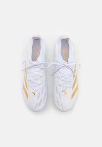 Valkoiset urheilukengät, joissa on hienovarainen tekstuurinen muotoilu, kultaiset yksityiskohdat ja kolme raitaa. Nauhat ovat valkoiset ja sisäpohjassa on kuvio.