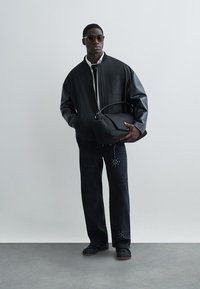 Czarna kurtka typu bomber z usztywnianymi skórzanymi rękawami, czarne dżinsy z ćwiekami oraz czarna torba na ramię. Modelka nosi okulary przeciwsłoneczne.