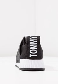 Czarne sneakersy z siateczkową cholewą, białą gumową podeszwą i wyraźnym logo "TOMMY" na tyle. Posiadają wycięcia dla lepszej wentylacji.