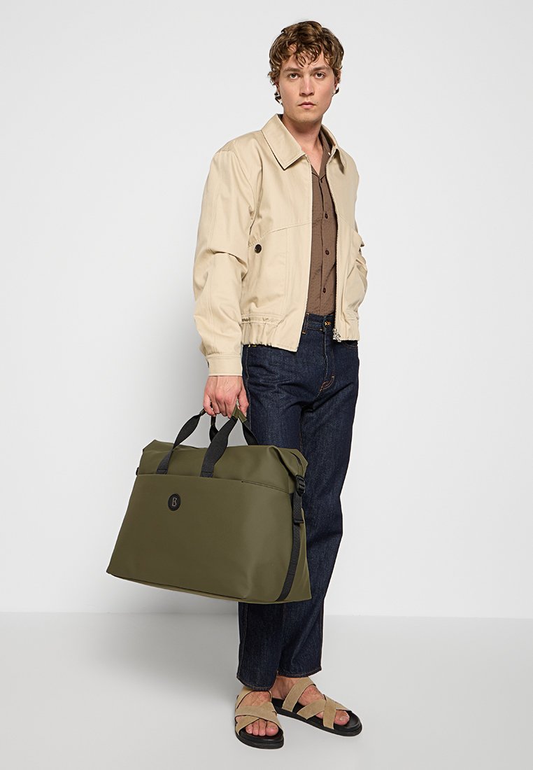 Olivgrüner, strapazierfähiger Stoffbeutel mit schwarzen Akzenten, Tragegriffen und einem Logopatch. Einfaches, strukturiertes Design für vielseitige Verwendung.