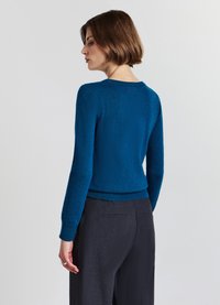Blauer Strickpullover mit Rundhalsausschnitt, gerippten Bündchen und Saum, kombiniert mit dunklen Hosen. Weiche Textur, taillierter Schnitt mit langen Ärmeln.