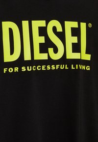 Černé bavlněné tričko s výrazným žlutým textem "DIESEL" a frází "PRO ÚSPĚŠNÝ ŽIVOT" v menším písmu pod ním.