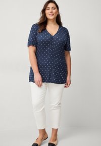 Námořnická halenka s puntíky, má výstřih do V, krátké nabírané rukávy a na přední straně nabírání, doplněná o bílé slim-fit kalhoty a béžové baleríny.