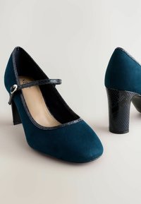 Teal mockaskinnklackar med rund tå, som har ett svart texturerat band och en glansig finish på klacken, accentuerad med ett ormskinnsmönster.