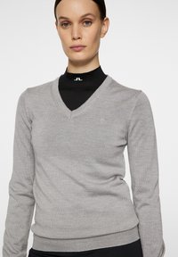 Harmaa v-pääntie neulepaita, joka on valmistettu pehmeästä, ribbausmateriaalista. Siinä on pitkät hihat ja istuva muotoilu, sekä pieni logo rintakehällä.