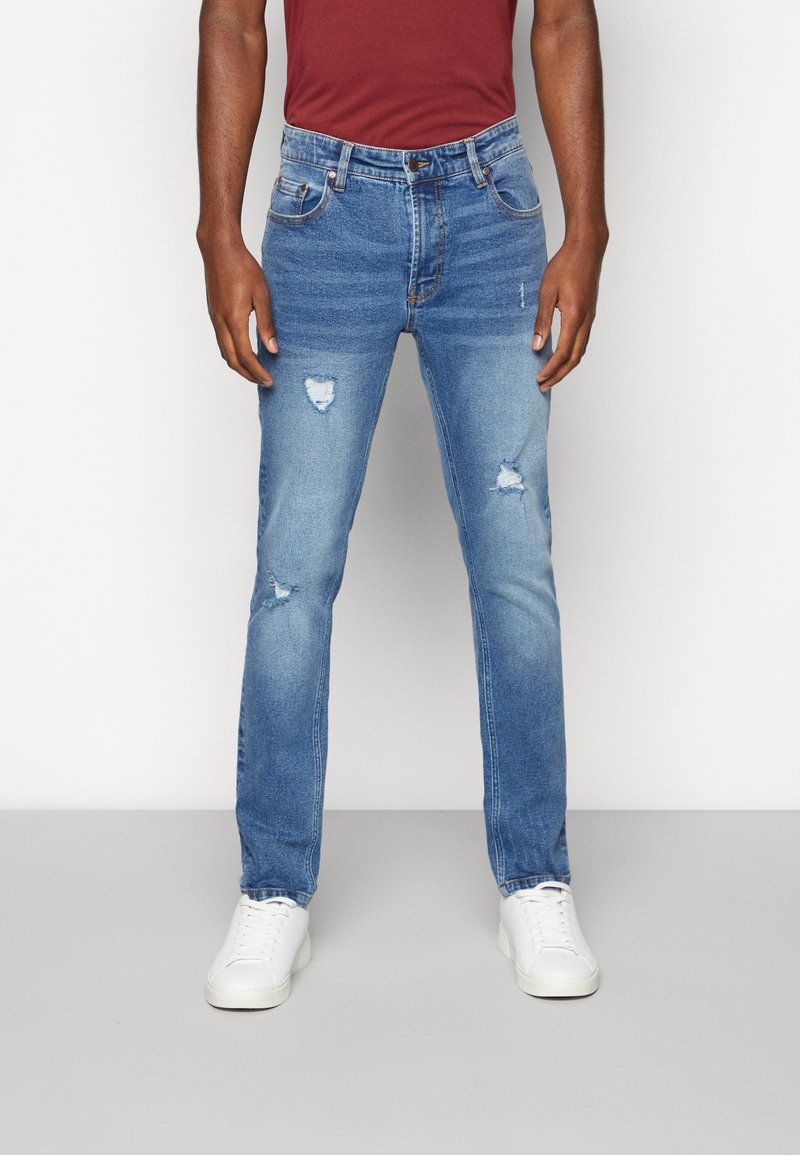 Blue denim jeans with a slim fit, featuring distressed details and a standard five-pocket design, paired with white sneakers.