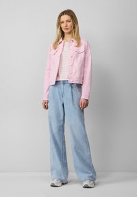 Roze spijkerjack met knopen aan de voorkant, gecombineerd met een gestreept lichtroze en wit topje. Losvallende, lichtblauwe broek met wijde pijpen en grijze sneakers.