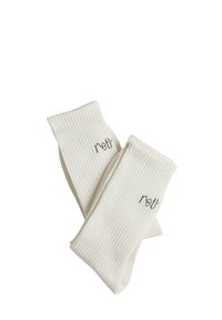 Chaussettes blanches côtelées à texture douce, ornées d'un petit logo "retr" brodé en gris près du haut.