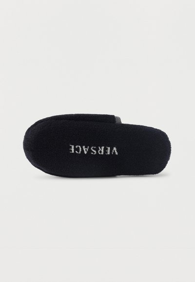 Μαύρο παντόφλα από περκάλι με ανοιχτή πλάτη και λευκό κεντημένο λογότυπο "VERSACE" στην επάνω σόλα, σε απλή φόντο.