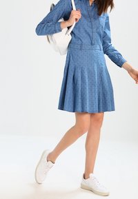 Jeansklänning med åtsittande liv, plisserad kjol och små prickar. Tillsammans med vita sneakers och en vit ryggsäck.