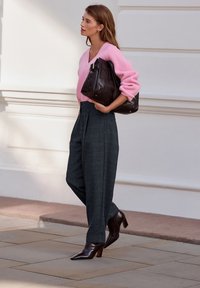 Roze geribbelde trui, grijze geruite hoge taille broek en een bruine leren handtas. De outfit wordt compleet gemaakt door bruine laarsjes met een spitse neus en hak.