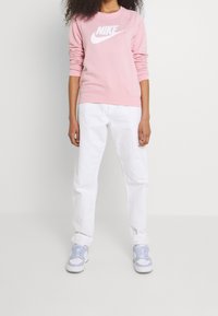 Rosa sweatshirt med vitt Nike-logotyp, kombinerad med vita byxor och ljusblå sneakers. Mjukt tyg med avslappnad passform och ribbade muddar.