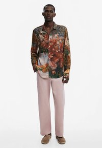 Floral print long-sleeve shirt in vibrant colors, featuring a button-down front and soft fabric; paired with straight, pale pink trousers.