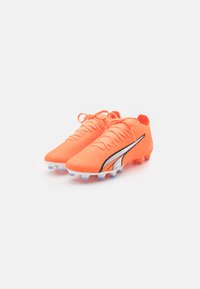 Scarpe da calcio di un vivace arancione con una tomaia testurizzata, caratterizzate da dettagli neri e argentati, e una suola bianca e blu.