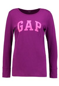 Lila långärmad t-shirt i bomull, med en stor rosa "GAP"-logotyp på framsidan och rund halsringning med uppvikta ärmar.
