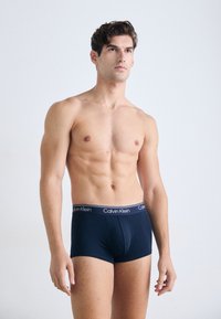 Marineblaue Baumwoll-Boxershorts mit einem Calvin Klein Logo-Bund. Glatte Textur und enganliegendes Design, präsentiert von einem männlichen Model.