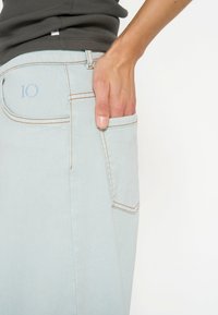 Jeans in denim blu chiaro con cuciture visibili, una tasca posteriore e un piccolo numero 10 ricamato. Tessuto liscio e design slim fit.