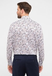 Camicia a maniche lunghe con motivo floreale in tonalità di bianco, blu, rosso e marrone, dotata di colletto classico e chiusura a bottoni sul retro.