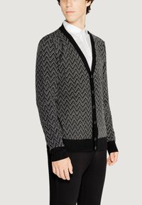 Cardigan a zigzag bianco e nero con scollo a V, chiusura con bottoni e polsini a coste, realizzato in tessuto lavorato a maglia.
